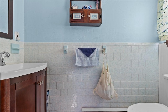 bathroom featuring toilet, tile walls, wainscoting, and vanity