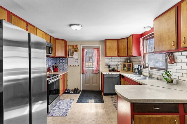 kitchen with a sink, decorative backsplash, light countertops, appliances with stainless steel finishes, and brown cabinets