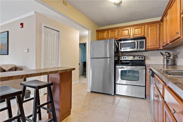 kitchen featuring brown cabinets, a kitchen breakfast bar, backsplash, stainless steel appliances, and light tile patterned floors