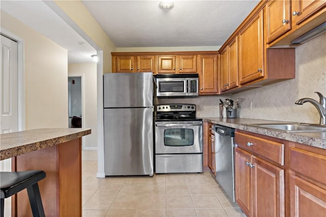 kitchen featuring a sink, stainless steel appliances, brown cabinetry, and light tile patterned floors