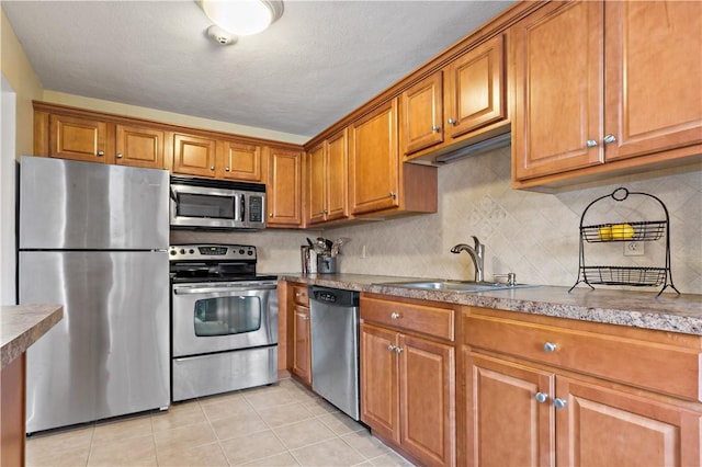 kitchen with a sink, light tile patterned flooring, brown cabinets, and stainless steel appliances