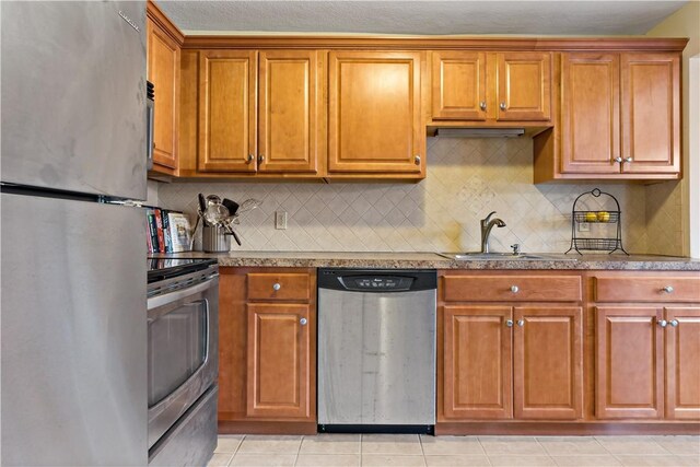 kitchen with light tile patterned floors, brown cabinets, stainless steel appliances, and a sink