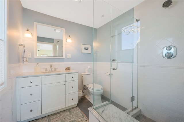 bathroom featuring a wainscoted wall, toilet, tile walls, a shower stall, and vanity