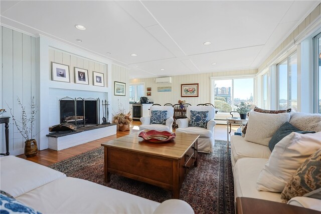 living area featuring a wall mounted air conditioner, a fireplace with raised hearth, wood finished floors, and recessed lighting