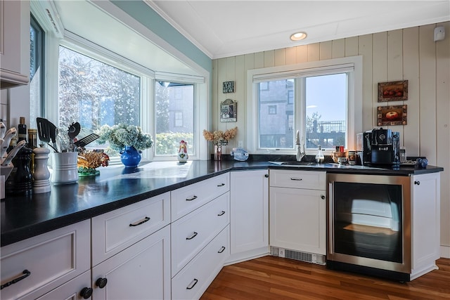 kitchen with dark wood finished floors, dark countertops, beverage cooler, and crown molding