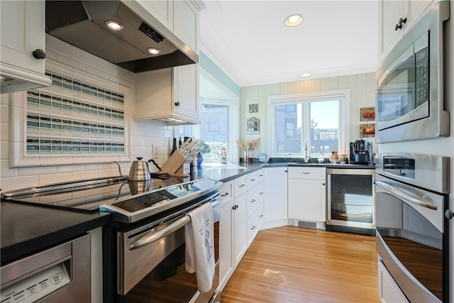 kitchen featuring beverage cooler, appliances with stainless steel finishes, dark countertops, and exhaust hood