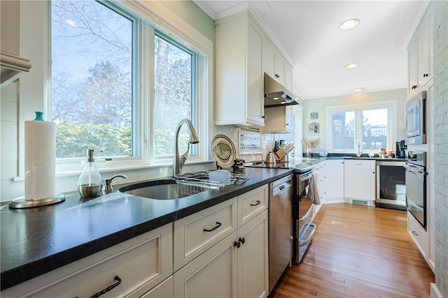 kitchen with under cabinet range hood, a sink, dark countertops, white cabinetry, and stainless steel appliances