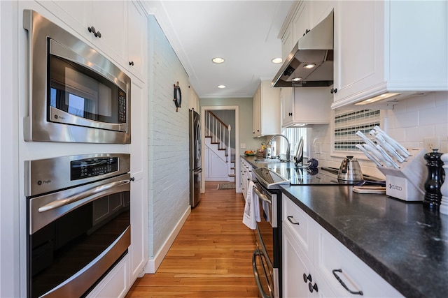 kitchen featuring under cabinet range hood, a sink, white cabinetry, appliances with stainless steel finishes, and light wood finished floors