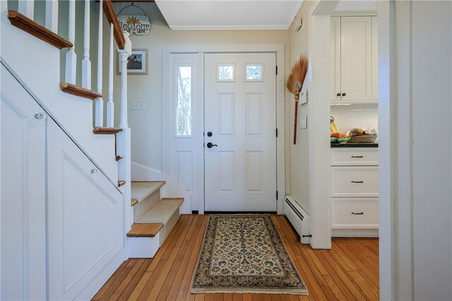 foyer entrance with light wood-type flooring, a baseboard radiator, crown molding, and stairway