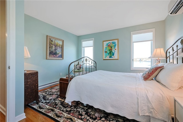 bedroom featuring a baseboard heating unit, wood finished floors, and a wall mounted air conditioner