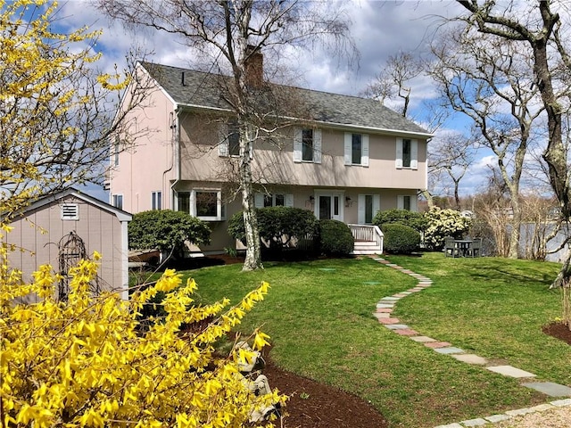 view of front of property featuring roof with shingles, a front yard, stucco siding, a chimney, and an outdoor structure