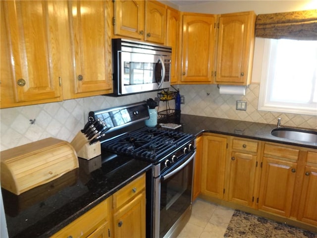 kitchen with tasteful backsplash, dark stone counters, brown cabinets, stainless steel appliances, and a sink