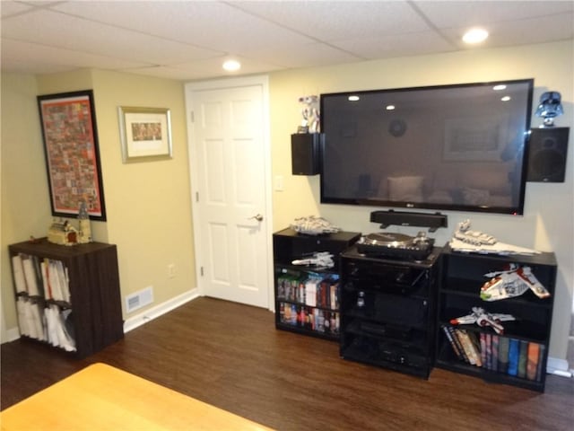 living area with wood finished floors, visible vents, a drop ceiling, and baseboards