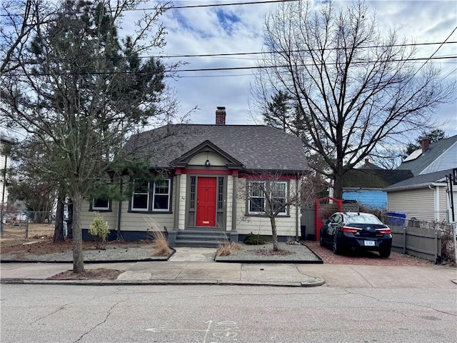 bungalow-style house with fence, roof with shingles, and a chimney