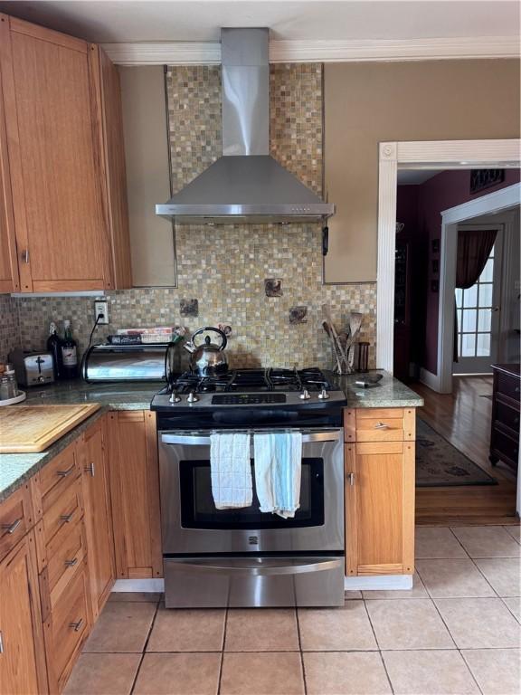 kitchen with stainless steel gas range oven, crown molding, wall chimney range hood, light tile patterned floors, and decorative backsplash