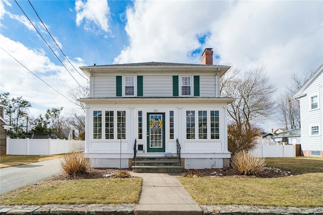 traditional style home with entry steps, a chimney, a front lawn, and fence