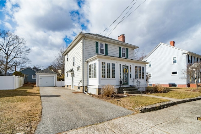 traditional style home featuring fence, aphalt driveway, a chimney, a garage, and an outbuilding