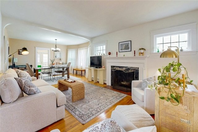 living room with a high end fireplace, a notable chandelier, and light wood-style floors