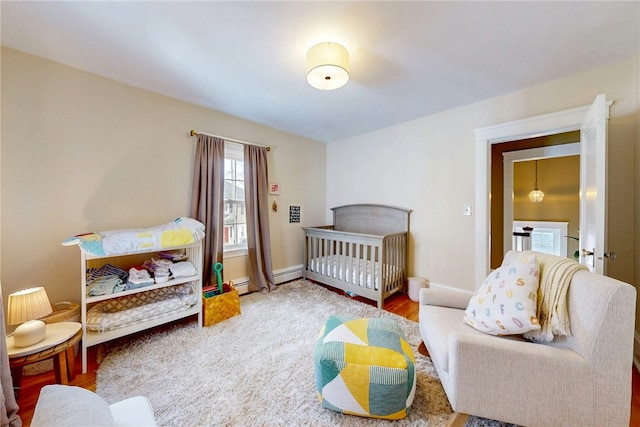 bedroom with a baseboard heating unit, a nursery area, wood finished floors, and baseboards