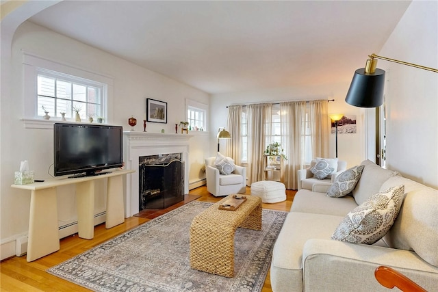 living room featuring baseboard heating, a fireplace, and light wood-style floors