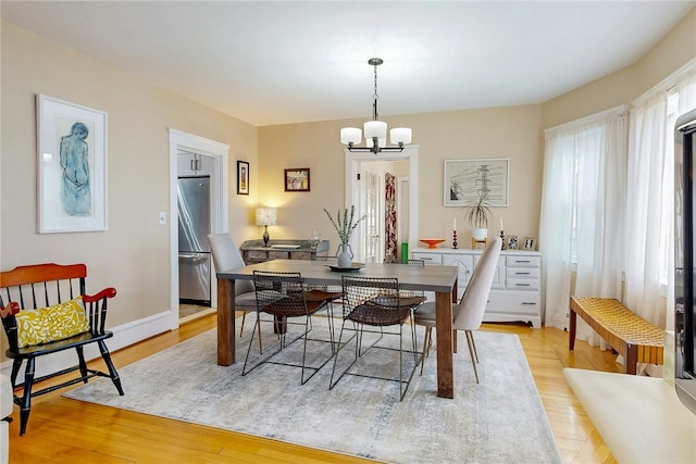 dining space with light wood finished floors, baseboards, and an inviting chandelier