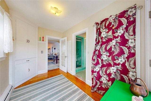 corridor featuring a baseboard radiator, baseboards, french doors, and light wood finished floors