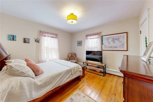 bedroom with light wood finished floors and a baseboard heating unit