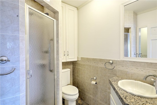 bathroom featuring a shower stall, crown molding, toilet, vanity, and tile walls