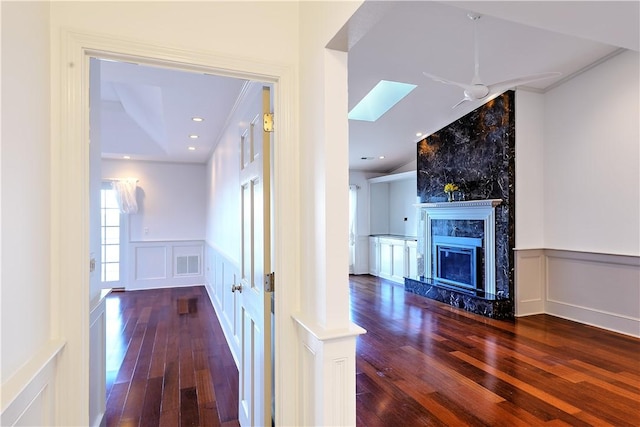 corridor with hardwood / wood-style floors, a decorative wall, visible vents, and wainscoting