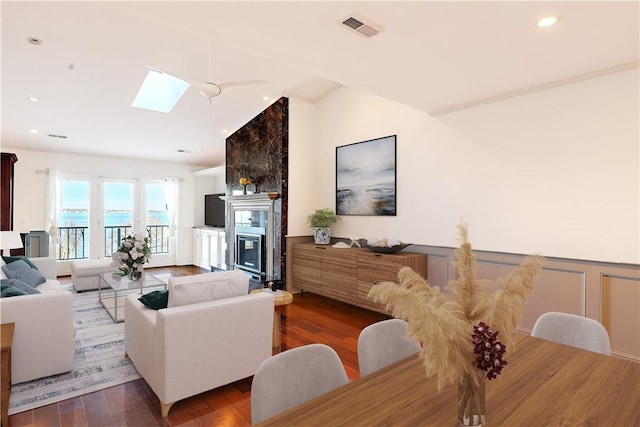 living room with visible vents, wainscoting, a skylight, wood finished floors, and a glass covered fireplace