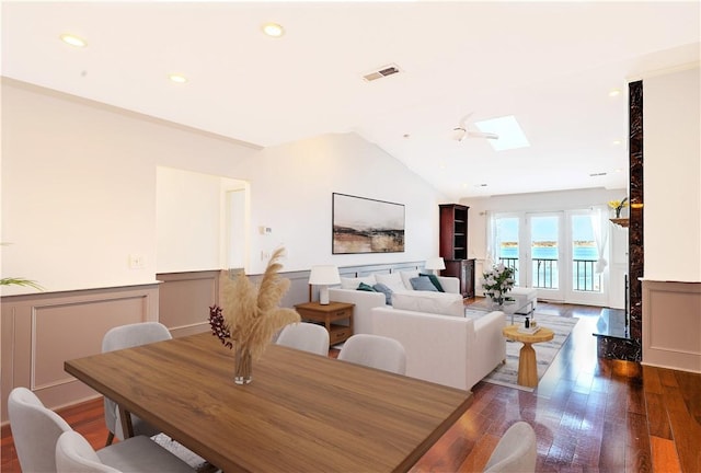 dining room with visible vents, vaulted ceiling with skylight, wood-type flooring, and a wainscoted wall