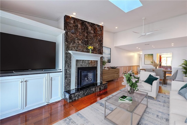 living area with ornamental molding, wood finished floors, recessed lighting, a skylight, and a premium fireplace