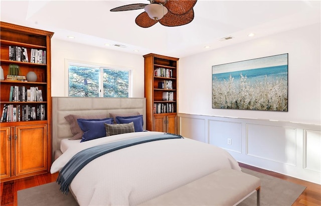 bedroom with visible vents, wainscoting, a decorative wall, and wood finished floors