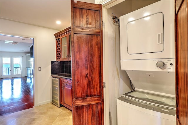 laundry area featuring beverage cooler, baseboards, laundry area, light tile patterned flooring, and stacked washer / drying machine