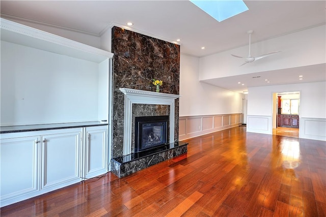 living area with a wainscoted wall, a skylight, a fireplace, hardwood / wood-style flooring, and a decorative wall