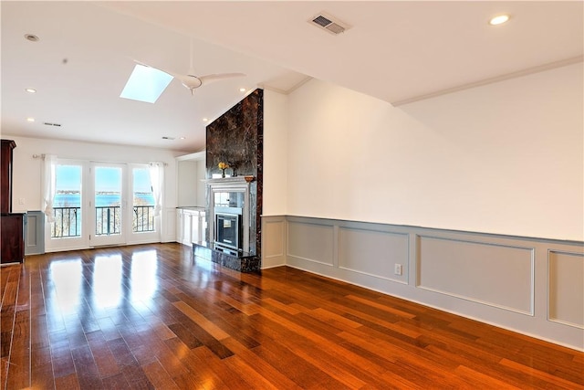 unfurnished living room with wood finished floors, visible vents, a skylight, recessed lighting, and a glass covered fireplace