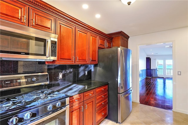 kitchen featuring baseboards, dark stone counters, light tile patterned flooring, decorative backsplash, and appliances with stainless steel finishes