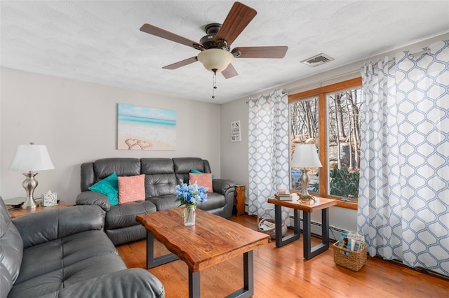 living room featuring visible vents, a baseboard heating unit, a ceiling fan, and light wood finished floors