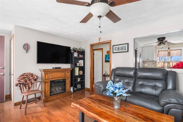 living room featuring a glass covered fireplace, baseboards, light wood-type flooring, and ceiling fan