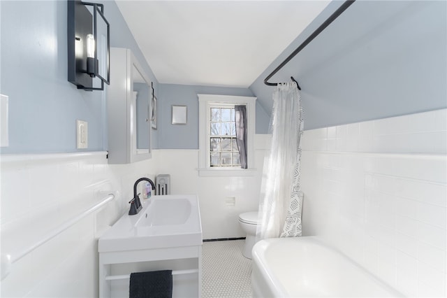 bathroom featuring a sink, a wainscoted wall, toilet, and tile walls