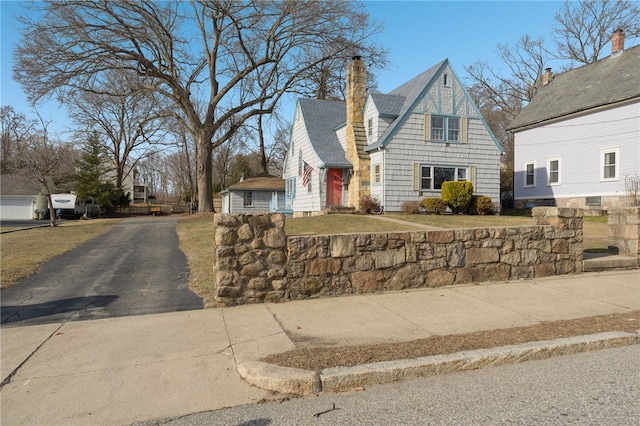 view of front of house with driveway, a front yard, roof with shingles, and a chimney