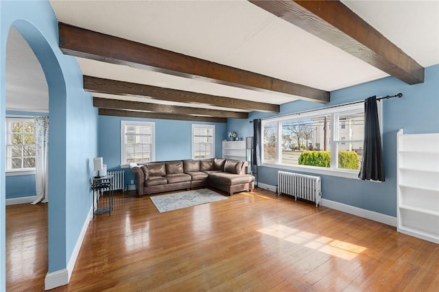 unfurnished living room featuring radiator, wood finished floors, arched walkways, and baseboards