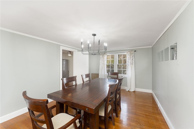 dining area with light wood-type flooring, baseboards, an inviting chandelier, and ornamental molding