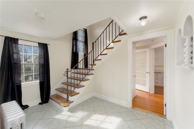 tiled entrance foyer with arched walkways, baseboards, radiator, and stairs