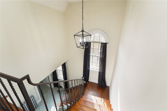 staircase with baseboards, wood finished floors, high vaulted ceiling, and a chandelier