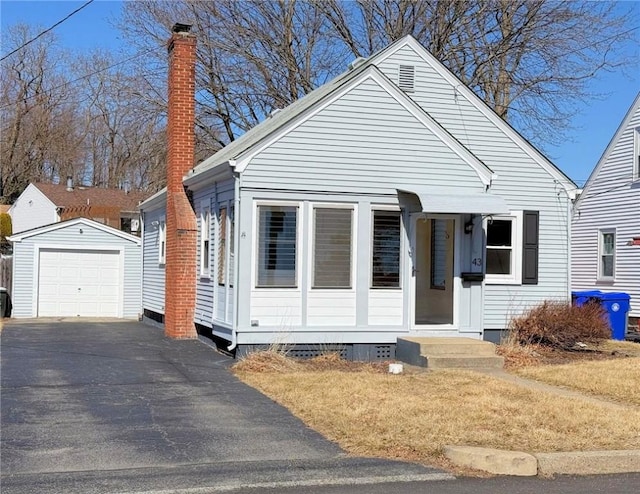 bungalow featuring an outdoor structure, a chimney, a detached garage, and aphalt driveway