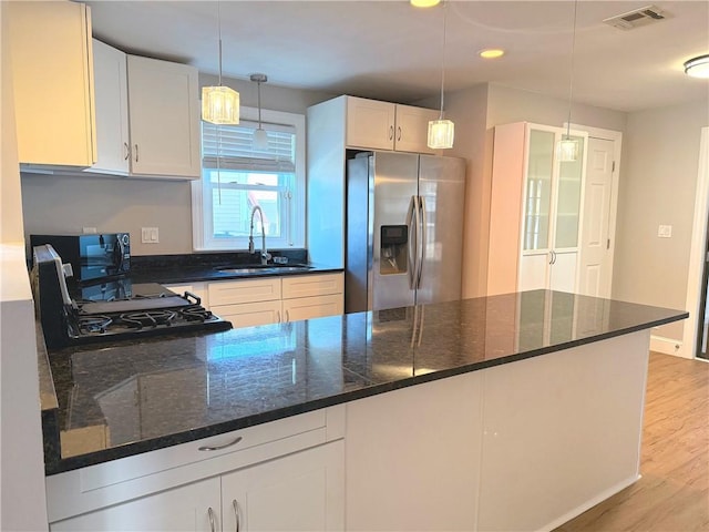 kitchen featuring visible vents, stainless steel refrigerator with ice dispenser, a sink, light wood finished floors, and range