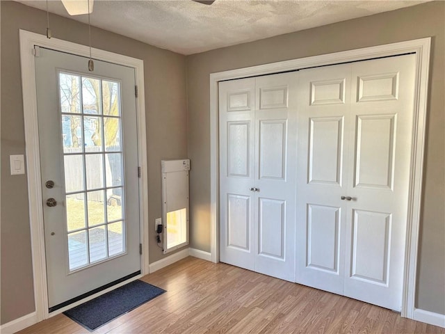 entryway with light wood-type flooring, baseboards, and a textured ceiling