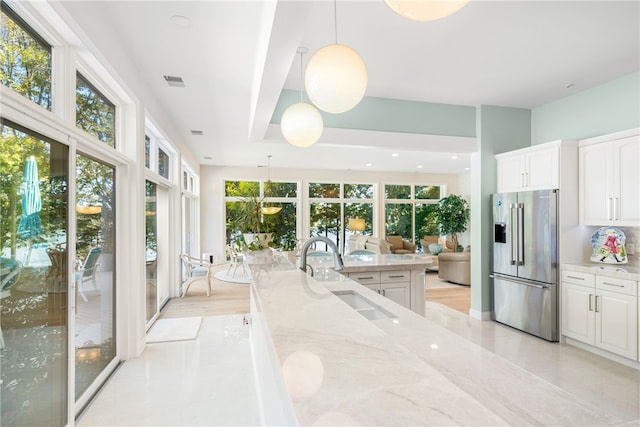 kitchen with visible vents, light stone countertops, high end fridge, white cabinetry, and a sink