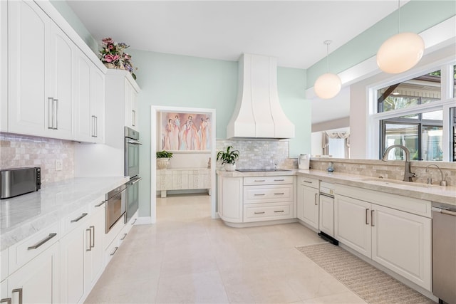 kitchen with light stone countertops, custom range hood, appliances with stainless steel finishes, white cabinetry, and a sink